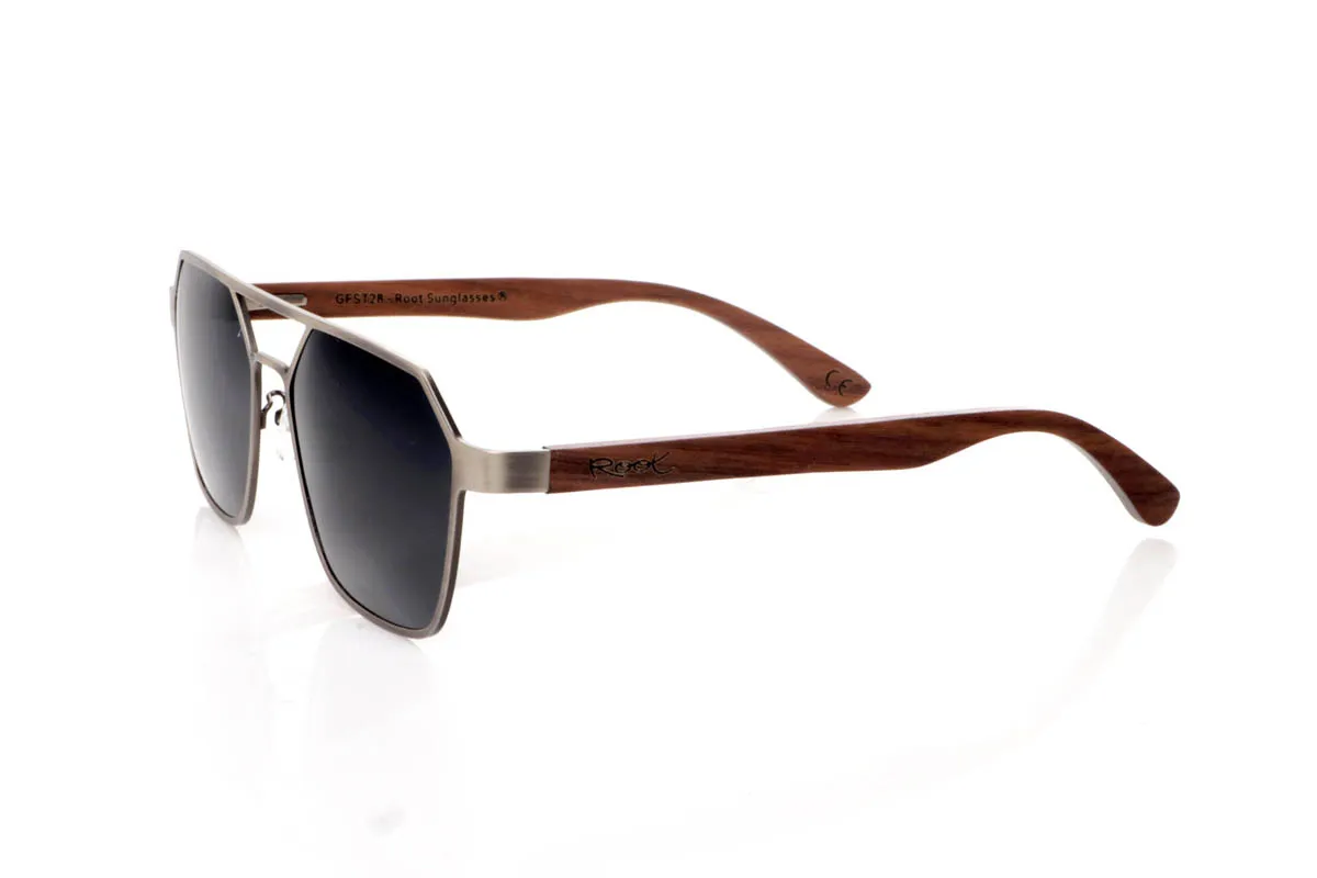 Gafas de Madera Natural de Walnut IBON. Las gafas de sol <b>IBON</b> combinan un frontal metálico de líneas geométricas con varillas de madera de walnut, creando una mezcla sofisticada entre diseño moderno y calidez natural. Su forma angular, con doble puente abierto y estructura ligera al aire, aporta un estilo atrevido y muy actual, ideal para quienes buscan unas gafas con presencia sin resultar pesadas. Las varillas de madera, finas y curvadas, muestran vetas naturales que hacen que cada par sea único y aportan comodidad durante el uso diario. Equipadas con lentes polarizadas que reducen los reflejos y protegen eficazmente frente a los rayos UV, son unas gafas diferentes, elegantes y con carácter propio. Medidas: 145x50 mm. Calibre 54. Venta al Por Mayor y Detalle | Root Sunglasses® 